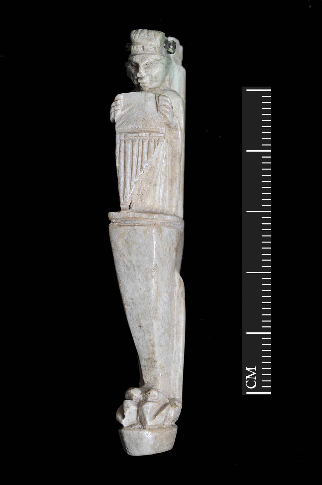 A carved bone handle for a folding knife. It depicts a grotesque figure holding a set of pan-pipes which is probably the Roman god Pan or another part-animal follower of the god Dionysus. Found during excavations for the Shires Shopping Centre - University of Leicester Archaeological Services
