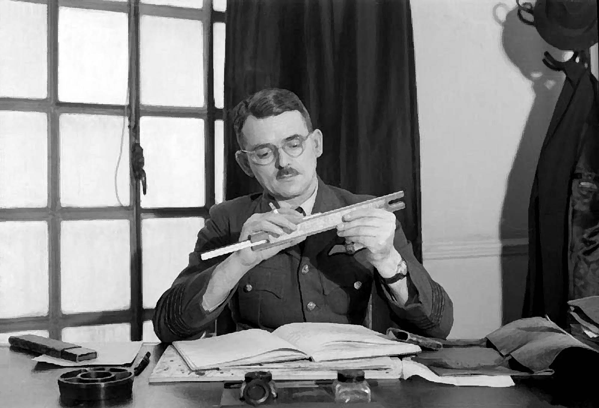 Frank Whittle adjusts a slide rule while seated at his desk at the Ministry of Aircraft Production - Imperial War Museums